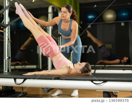 Female trainer guiding girl doing pelvic lift exercise on reformer Female trainer guiding girl doing pelvic lift exercise on reformer 136599370