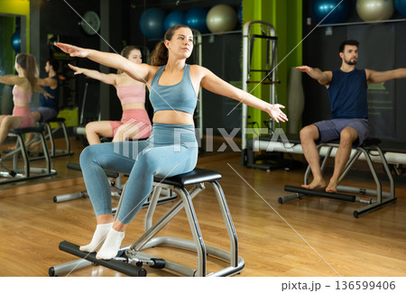 Woman doing arm and leg exercises on chair in Pilates class 136599406