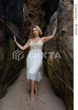 Blonde woman in white dress standing between rocks Blonde woman in white dress standing between rocks 136599472
