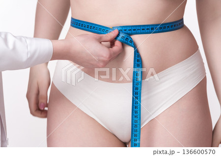 A close-up of a doctor's hand meticulously measuring the dimensions of a patient's waist using a measuring tape. A perfect illustration of the dedication and skill involved in the medical process 136600570