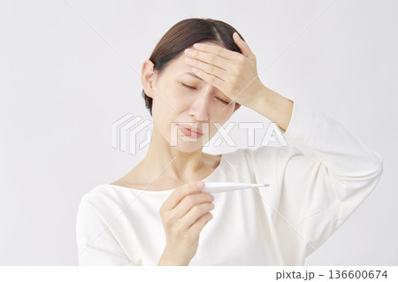 体温計で体温を測る女性 白背景 体温計で体温を測る女性 白背景 136600674