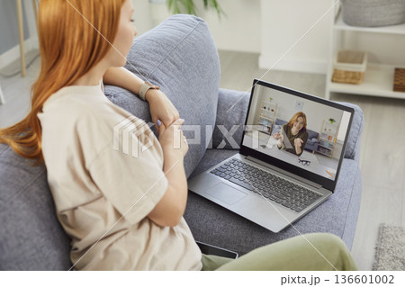 Young attractive millennial red-haired girl having home talk on laptop video call with friend Young attractive millennial red-haired girl having home talk on laptop video call with friend 136601002