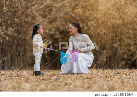 Mother and child girl bonding while playing with butterfly nets in dry forest. Mother and child girl bonding while playing with butterfly nets in dry forest. 136601664
