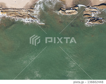 Waves touch rocky shore near sandy beach in bright sunlight Waves touch rocky shore near sandy beach in bright sunlight 136602448