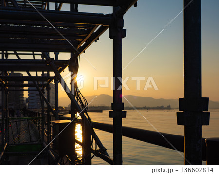 海辺の足場越しに沈む夕日 逆光シルエットの港風景 海辺の足場越しに沈む夕日 逆光シルエットの港風景 136602814