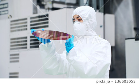 半導体工場でシリコンウエハーを検査する防塵服を着た男性作業員 136603055