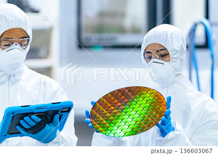 半導体工場でタブレットを持ってシリコンウエハーを検査する防護服を着た男女作業員 136603067