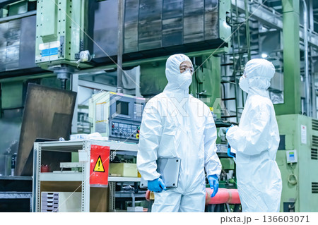 防護服を着て工場の中で話す男女作業員 防護服を着て工場の中で話す男女作業員 136603071