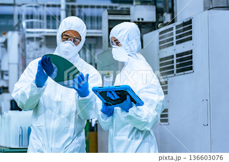 半導体工場でタブレットを持ってシリコンウエハーを検査する防護服を着た男女作業員 136603076
