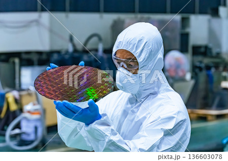 半導体工場でシリコンウエハーを検査する防護服を着た男性作業員 半導体工場でシリコンウエハーを検査する防護服を着た男性作業員 136603078