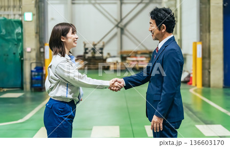 工場の中で握手する男性ビジネスパーソンと女性作業員 136603170