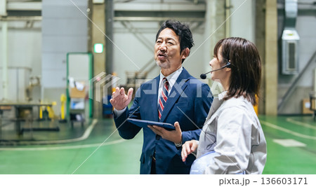 工場を視察する男性ビジネスパーソンと女性作業員 136603171
