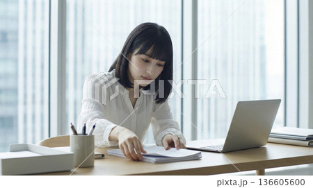 デスクで書類を整理しながらPC作業をする日本人女性 136605600
