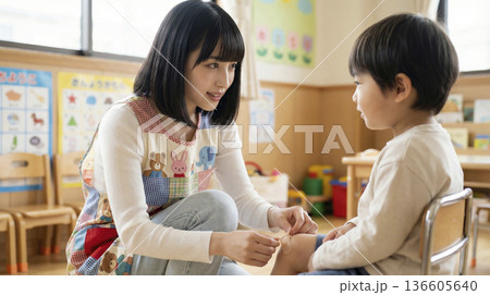 保育園でケガをした園児の膝に絆創膏を貼る日本人保育士 136605640