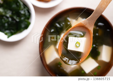 Close up of wooden spoon scooping miso soup with soft tofu and seaweed from a wooden bowl, Top view Close up of wooden spoon scooping miso soup with soft tofu and seaweed from a wooden bowl, Top view 136605715