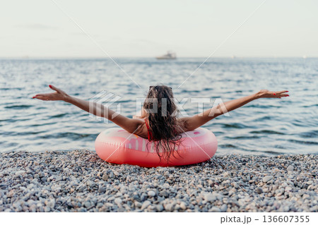 Woman, beach, sea. Relaxing on a pebble beach, a woman enjoys her summer vacation, arms outstretched in freedom. 136607355