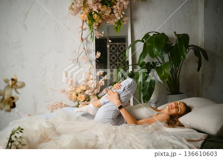 Woman lies on a bed surrounded by plants and flowers in a bright indoor space Woman lies on a bed surrounded by plants and flowers in a bright indoor space 136610603