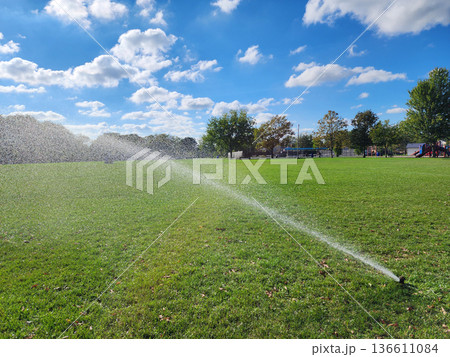 Automatic lawn sprinkler watering green grass. Water sprinklers watering soccer field. Football field irrigation. Irrigation turf. Sprinkler watering football field. Football turf irrigation Automatic lawn sprinkler watering green grass. Water sprinklers watering soccer field. Football field irrigation. Irrigation turf. Sprinkler watering football field. Football turf irrigation 136611084