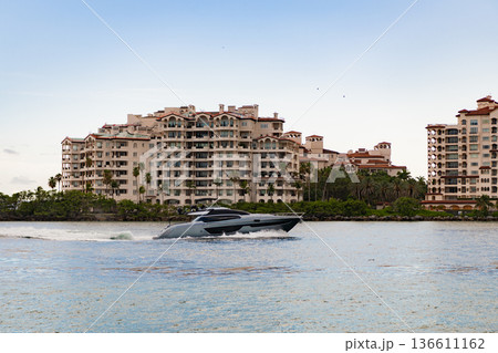 Vacation on summer. Fisher island building. Luxury boat motor yacht. Luxury yacht go to marina. Boating and yachting. Luxury lifestyle. Yacht at Fisher island luxury residential building 136611162
