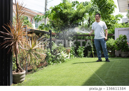 A calm man waters plants with focus and care in his home garden. The moment expresses mindfulness, patience, and connection with nature. A calm man waters plants with focus and care in his home garden. The moment expresses mindfulness, patience, and connection with nature. 136611384