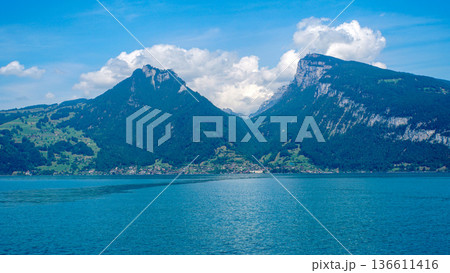 スイスのトゥーン湖の青い水面と、背後にそびえ立つ緑豊かなアルプスの山々が作り出す夏の風景 136611416