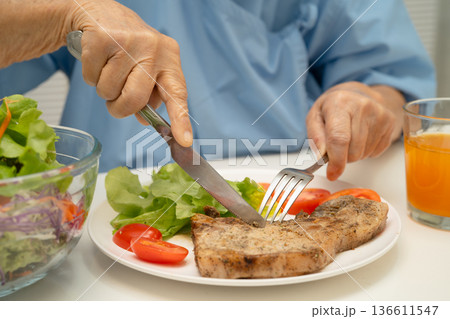 Asian elderly woman patient eating pork chop stake and vegetable salad for healthy food in hospital. Asian elderly woman patient eating pork chop stake and vegetable salad for healthy food in hospital. 136611547