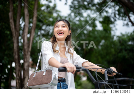 Pretty asian woman smiling broadly while riding a bicycle strolling around in the nature park. Pretty asian woman smiling broadly while riding a bicycle strolling around in the nature park. 136613045