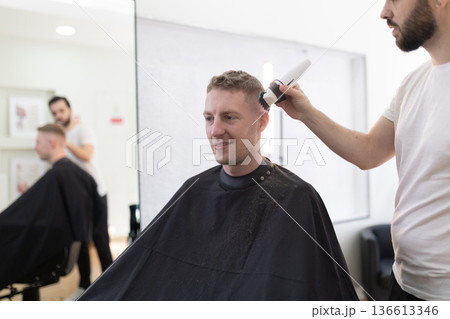Client getting modern haircut from barber in salon 136613346