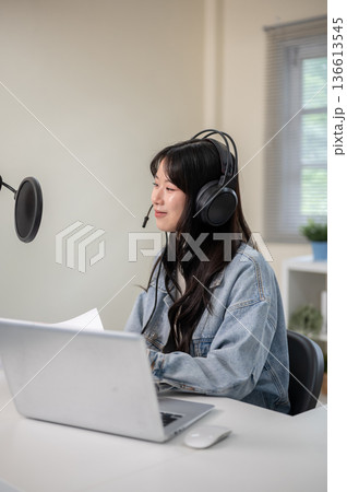 Asian woman hosting a radio show or podcast through laptop with headset and mic at home or studio. Asian woman hosting a radio show or podcast through laptop with headset and mic at home or studio. 136613545