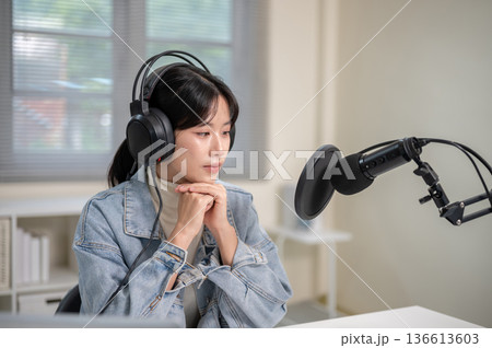 Asian woman with mic headset clasping hands while hosting a radio show or podcast at home or studio. Asian woman with mic headset clasping hands while hosting a radio show or podcast at home or studio. 136613603
