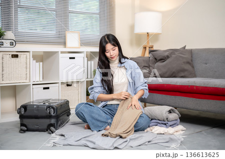 Asian woman folding a cloth packing or organizing luggage for trip on bedroom or living room floor. 136613625
