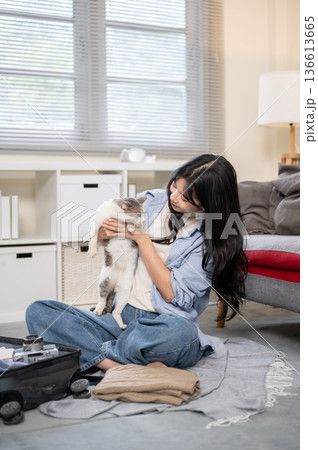 Asian woman holding a cat while organize or packing the luggage on bedroom or living room's floor. 136613665