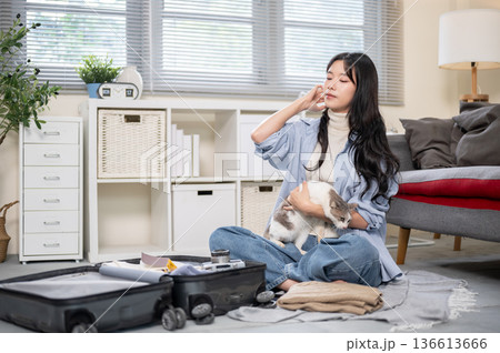 Asian woman holding a cat while organize or packing her luggage on a bedroom or living room's floor. 136613666