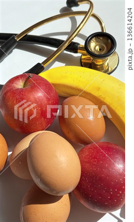 Health Promotion With Fruits And Medical Tools. Symbolic Health Care Setup Featuring Fruits And Medical Instruments Against White Background 136614204