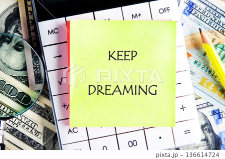 Bright yellow sticky note with the words Keep Dreaming placed on a calculator surrounded by cash and a magnifying glass sets a motivational scene for ambition Bright yellow sticky note with the words Keep Dreaming placed on a calculator surrounded by cash and a magnifying glass sets a motivational scene for ambition 136614724