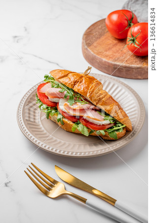 Croissant sandwich with ham, mozzarella cheese and arugula on a plate on a marble background Croissant sandwich with ham, mozzarella cheese and arugula on a plate on a marble background 136614834