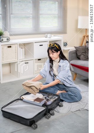 Asian woman putting folded cloth in a luggage while organizing or packing in bedroom or living room. Asian woman putting folded cloth in a luggage while organizing or packing in bedroom or living room. 136615037