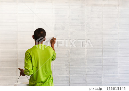 Man painting a house brick wall on textured surface with white color. Man painting a house brick wall on textured surface with white color. 136615143