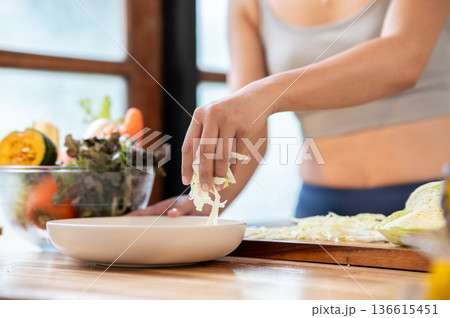 Close up of sportswear woman's hand putting shred cabbage into a plate at kitchen cooking counter. 136615451
