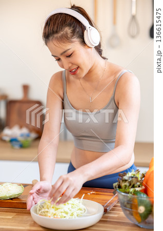 Asian woman in sportswear listening to music in headphone while cooking vegetable at kitchen counter Asian woman in sportswear listening to music in headphone while cooking vegetable at kitchen counter 136615475