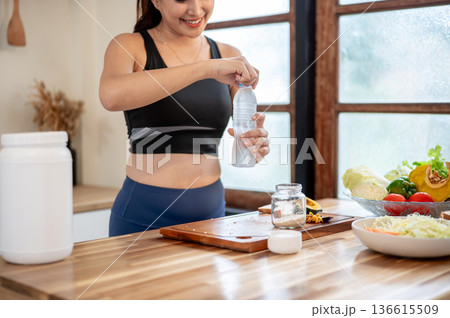 Close up of woman holding water making protein powder shake drink in jar at kitchen cooking counter. 136615509