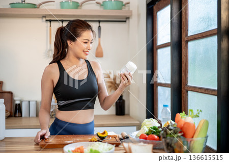 Happy asian woman holding a glass jar making protein powder shake drink at kitchen cooking counter. Happy asian woman holding a glass jar making protein powder shake drink at kitchen cooking counter. 136615515