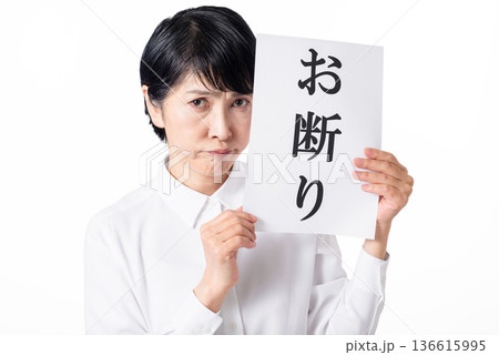 お断りと書かれた紙を持ち口をとがらせる白いシャツを着たシニア女性 お断りと書かれた紙を持ち口をとがらせる白いシャツを着たシニア女性 136615995