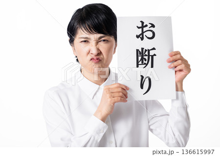お断りと書かれた紙を持ち嫌そうな表情の白いシャツを着たシニア女性 お断りと書かれた紙を持ち嫌そうな表情の白いシャツを着たシニア女性 136615997