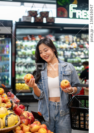 Asian woman standing holding shopping basket looking or buying apple at fruit section in supermarket 136616047