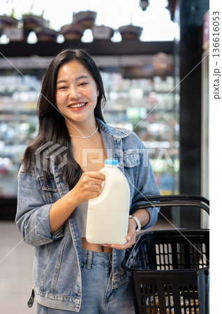 Asian woman holding shopping basket and buying or choosing a milk gallon from fridge in supermarket. Asian woman holding shopping basket and buying or choosing a milk gallon from fridge in supermarket. 136616053