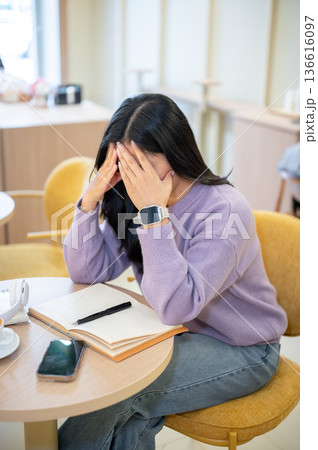 Asian woman holding head getting tired after long hours working or study as sitting at table in cafe 136616097