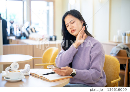 Asian woman holding phone wiping neck sweat checking unwell temperature as sitting at table in cafe. 136616099