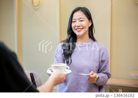 Barista serving coffee cup to woman customer standing and paying with credit card at cafe's counter 136616102