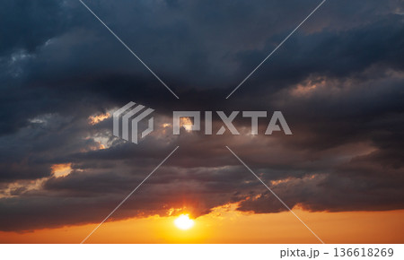 Dramatic dark clouds with sun rays breaking through sunset storm sky Dramatic dark clouds with sun rays breaking through sunset storm sky 136618269